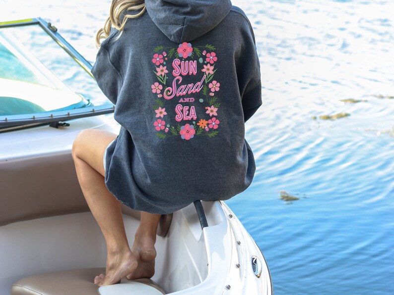 May include: A dark gray hooded sweatshirt with a floral design and the text "Sun Sand and Sea" on the back.