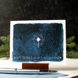 May include: A Christmas card with a blue watercolor background depicting a starry night sky with a white star in the center. The text "Happy Christmas to all and to all a good night" is printed in white at the bottom of the card.