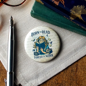 May include: A round button with the text "BORN TO READ" and "FORCED TO WORK" features a cartoon illustration of a person reading a book. The button has a vintage book page background and is surrounded by books and birds.