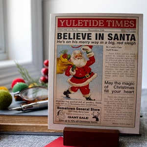 Pu&ograve; includere: Un'illustrazione di giornale vintage di Yuletide Times con Babbo Natale in un abito rosso e una grande slitta rossa, che consegna i regali. Il testo recita "Credi in Babbo Natale" e "&Egrave; in viaggio su una grande slitta rossa".