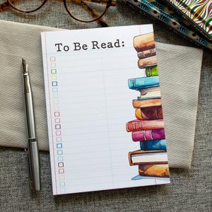 May include: A white notepad with blue lines and a stack of colorful books on the right side. The notepad has the words "To Be Read" at the top and a list of empty boxes.