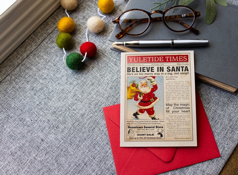 Pu&ograve; includere: Un ritaglio di giornale in stile vintage con un'illustrazione di cartone animato di Babbo Natale che porta un sacco di regali. Il titolo recita "YULETIDE TIMES CREDI IN BABBO NATALE &Egrave; in viaggio su una grande slitta rossa". Il testo include anche "Che la magia del Natale riempia il tuo cuore" e "Hometown General Store GRANDE SALDO Risparmia fino al 70% sugli articoli natalizi".
