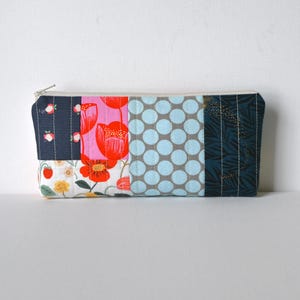 May include: A rectangular zippered pouch featuring a quilted patchwork design. The fabric panels include a dark navy with small floral motifs, a bright pink with red poppies, a white floral print with strawberries, light blue polka dots, and dark teal.