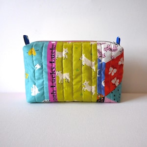 May include: A rectangular quilted zipper pouch featuring a patchwork design with various colorful patterns. The fabric includes a light blue section with yellow hearts, a pink strip with the text Ooh Lucky Lucky, a lime green panel with white goats, and a red section with white butterflies.
