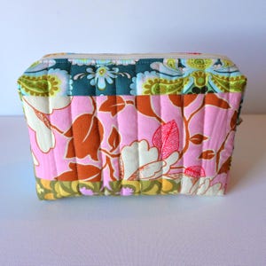 May include: A quilted cosmetic bag with a floral pattern in pink, brown, and white. The bag has a rectangular shape with a zipper closure and is made of fabric. The top section features a teal and green paisley design.