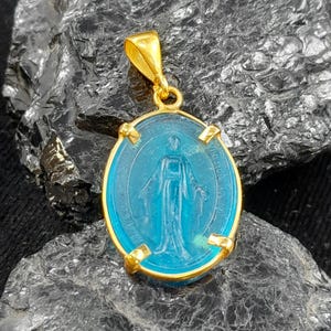 Puede incluir: Pendiente de oro con un camafeo ovalado de vidrio azul que representa a la Virgen Mar&iacute;a. El camafeo est&aacute; rodeado por un marco de oro con cuatro acentos decorativos.