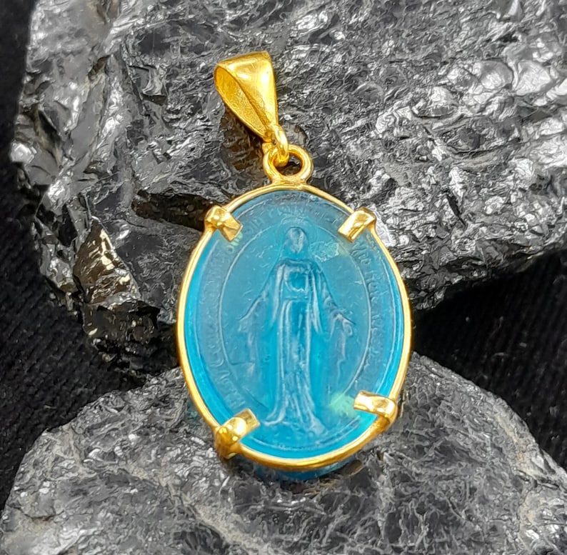 Puede incluir: Pendiente de oro con un camafeo ovalado de vidrio azul que representa a la Virgen Mar&iacute;a. El camafeo est&aacute; rodeado por un marco de oro con cuatro acentos decorativos.