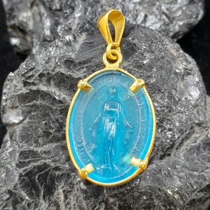 Puede incluir: Pendiente de oro con un camafeo de vidrio azul de la Virgen Mar&iacute;a. El camafeo tiene forma ovalada y tiene un marco de oro con cuatro acentos decorativos.