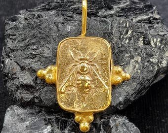 May include: A gold-toned pendant featuring a detailed bee design. The bee is centered on a rectangular plaque with rounded corners and decorative accents. The pendant is perfect for adding a touch of nature to any jewelry collection.