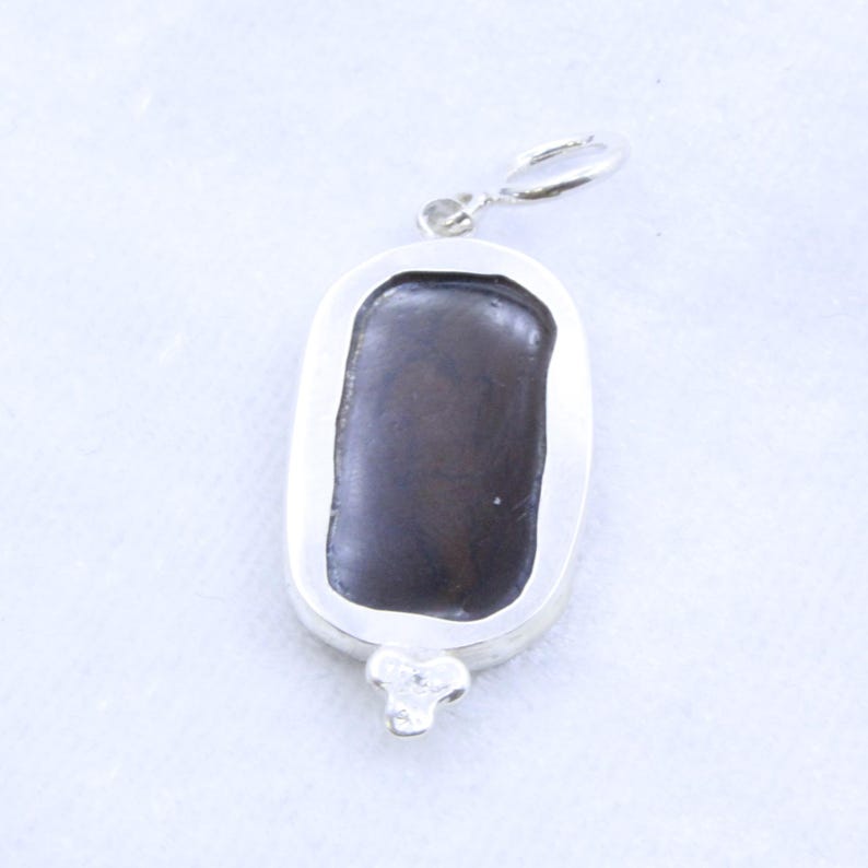 May include: A rectangular pendant with a dark brown center stone set in a silver-colored metal frame. The pendant has a loop at the top for a chain and a decorative three-petal design at the bottom.
