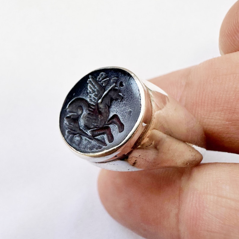 May include: A silver ring with a black onyx stone featuring a carved image of a winged horse.