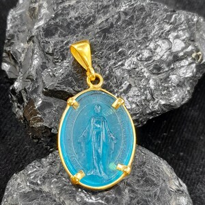 Puede incluir: Pendiente de oro con un &oacute;valo de vidrio azul que presenta una imagen de la Virgen Mar&iacute;a. El pendiente tiene una anilla de oro.