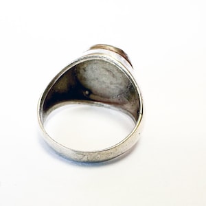May include: Silver ring with a round, smooth, gray stone set in the center. The ring is a simple design with a wide band.