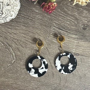 May include: A pair of black and white marbled circle earrings with gold crescent moon accents.