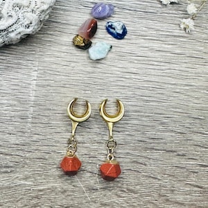 May include: A pair of gold crescent moon shaped ear gauges with red gemstone dangles.