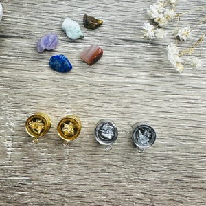 Könnte beinhalten: Vier Paar Ohrdehner, zwei golden und zwei silbern, mit verschiedenen Mustern. Die Dehnungen befinden sich auf einer Holzoberfläche.