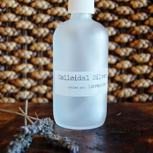 May include: A frosted glass bottle with a white spray top and a white label that reads "Colloidal Silver Infused with Lavender".