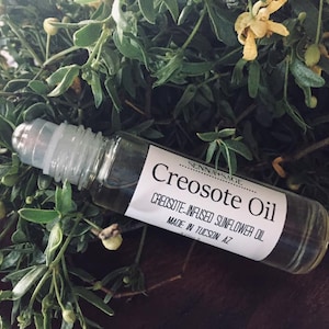 May include: A clear glass roll-on bottle with a white label that reads "Creosote Oil, Creosote-Infused Sunflower Oil, Made in Tucson, AZ".