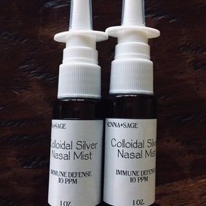 Könnte beinhalten: Zwei Flaschen SENNA+SAGE Kolloidales Silber Nasenspray. Jede Flasche hat eine weiße Düse und ein Etikett mit dem Text "IMMUNE DEFENSE 10 PPM" und "1 OZ.". Die Flaschen sind dunkelbraun.
