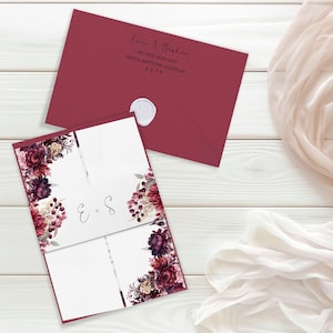 May include: Burgundy red wedding invitation with a white envelope. The invitation features a floral design with burgundy, white, and gray flowers. The text on the invitation reads "E + S".