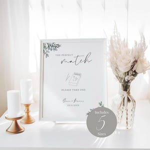 Peut inclure: Une pancarte blanche avec le texte "The Perfect Match" et un dessin d'une boîte d'allumettes avec des cœurs. La pancarte comprend également le texte "Please Take One" et la date "23.11.20XX". Un cercle blanc avec le texte "Includes 5 Sizes" se trouve dans le coin inférieur droit de l'image.