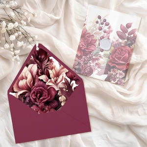 May include: A burgundy envelope with a floral design featuring burgundy, pink, and white flowers. The envelope is lying on a white surface.