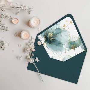 Könnte beinhalten: Ein blaugrüner Umschlag mit einem weißen Futter, das mit einem Aquarelldesign aus blauen Blumen mit goldenen Akzenten verziert ist.