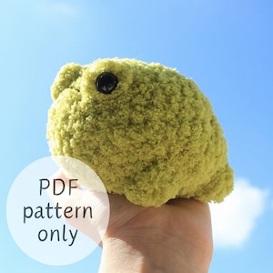 Könnte beinhalten: Ein grünes Plüsch-Froschspielzeug mit einem schwarzen Auge. Das Spielzeug wird in einer Hand vor einem blauen Himmel gehalten. Der Text "PDF pattern only" ist im Bild sichtbar.
