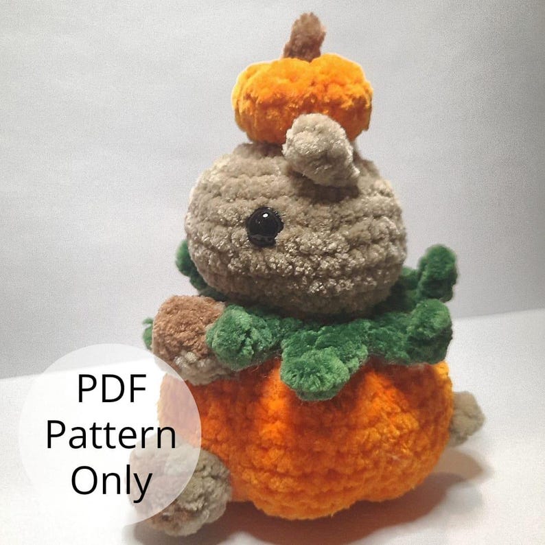 May include: Crochet pattern for a plush pumpkin with a small brown and gray creature wearing a green leaf crown and a smaller orange pumpkin on its head. The pattern is available as a PDF download.  PDF Pattern Only.