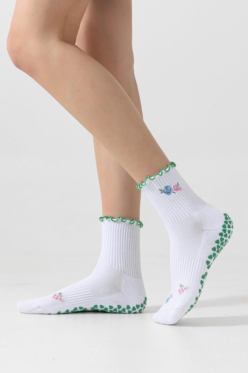 Puede incluir: Calcetines blancos hasta el tobillo con puntos antideslizantes verdes en la parte inferior y un volante verde y blanco en la parte superior. Los calcetines tienen un peque&ntilde;o dise&ntilde;o floral bordado en el lateral.