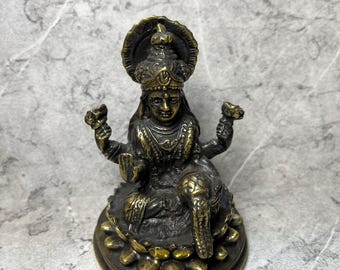 May include: A detailed bronze statue of a seated deity, adorned with intricate headwear and jewelry. The figure has multiple arms and is seated on a lotus flower base, with an elephant head visible. The statue has a detailed design and is a religious item.