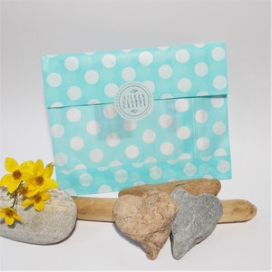 May include: A turquoise polka dot gift bag with a clear window and a round sticker that reads "Aileen Clarke Crafts". The bag is next to a gray stone, two heart-shaped stones, driftwood, and yellow flowers.
