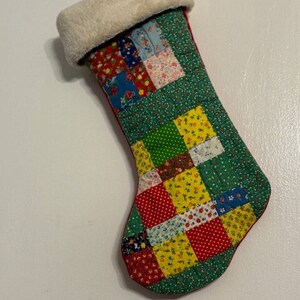 May include: A vintage patchwork Christmas stocking with a white faux fur cuff. The stocking is made of various colorful fabrics with floral and geometric patterns.