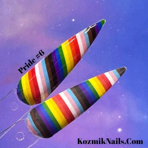 May include: Two long, thin, pointed nail tips with a rainbow stripe design. The stripes are in the colors of the Progress Pride flag, including black, brown, light blue, pink, white, yellow, green, turquoise, and red. The text "Pride #6" is written on the left side of the image.
