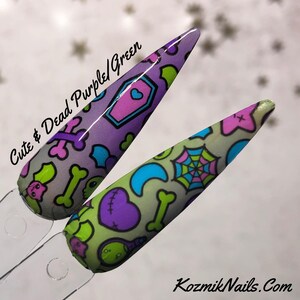 May include: Two long, pointed fake nails with a cute and spooky design. The nails are painted in a light purple and green base with a variety of small, colorful designs, including hearts, bones, stars, and a spider web. The text "Cute & Dead Purple/Green" is written on the image.