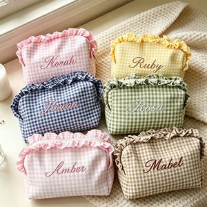 May include: Six rectangular zipped pouches with ruffled edges, each featuring a gingham pattern in pink, yellow, navy blue, green, or brown. Each pouch is embroidered with a unique name: Norah, Ruby, Rowan, Rosa, Amber, or Mabel.