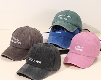 Puede incluir: Cinco gorras de béisbol en tonos marrón, negro, azul, verde y rosa. Cada gorra tiene texto bordado, incluyendo "Custom Embroidery", "Custom Text" y "Grandma EST. 2025."