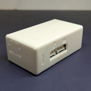 May include: A white rectangular electronic device with a smooth surface. The device has a slot with two connectors and a few small indentations. The device is on a dark blue surface.