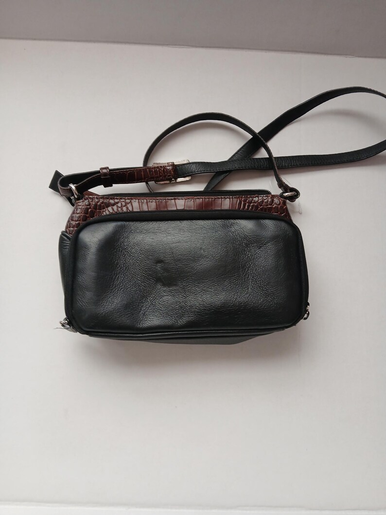 Pode incluir: Bolsa transversal de couro preto com uma se&ccedil;&atilde;o superior marrom texturizada. A bolsa tem uma al&ccedil;a longa e ajust&aacute;vel e uma al&ccedil;a mais curta. A bolsa &eacute; retangular e possui fecho de z&iacute;per.