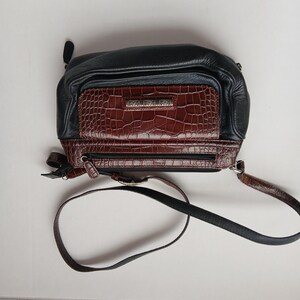 Pode incluir: Bolsa transversal preta e marrom com um bolso frontal de pele de crocodilo sint&eacute;tica. A bolsa tem uma parte superior de couro preto e uma al&ccedil;a longa e ajust&aacute;vel. A bolsa tem fecho de z&iacute;per e um pequeno la&ccedil;o na lateral.