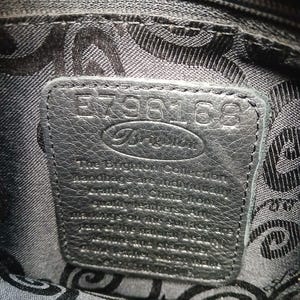 Pode incluir: Close-up do interior de uma mala de m&atilde;o de couro preto. Uma etiqueta retangular de couro &eacute; costurada no interior, com a marca "Brighton" e o n&uacute;mero de s&eacute;rie E798168 em relevo. O forro apresenta um padr&atilde;o repetitivo.