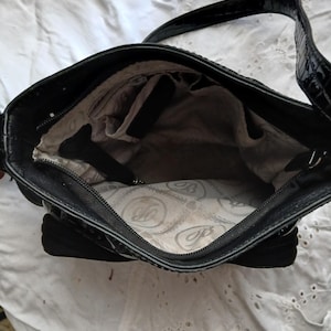 以下が含まれることがあります： 黒い革のハンドバッグ。表面はテクスチャ加工、持ち手は光沢があります。内側には複数のコンパートメントと模様入りの裏地があります。ジッパー開閉で、必需品を持ち運ぶように設計されています。