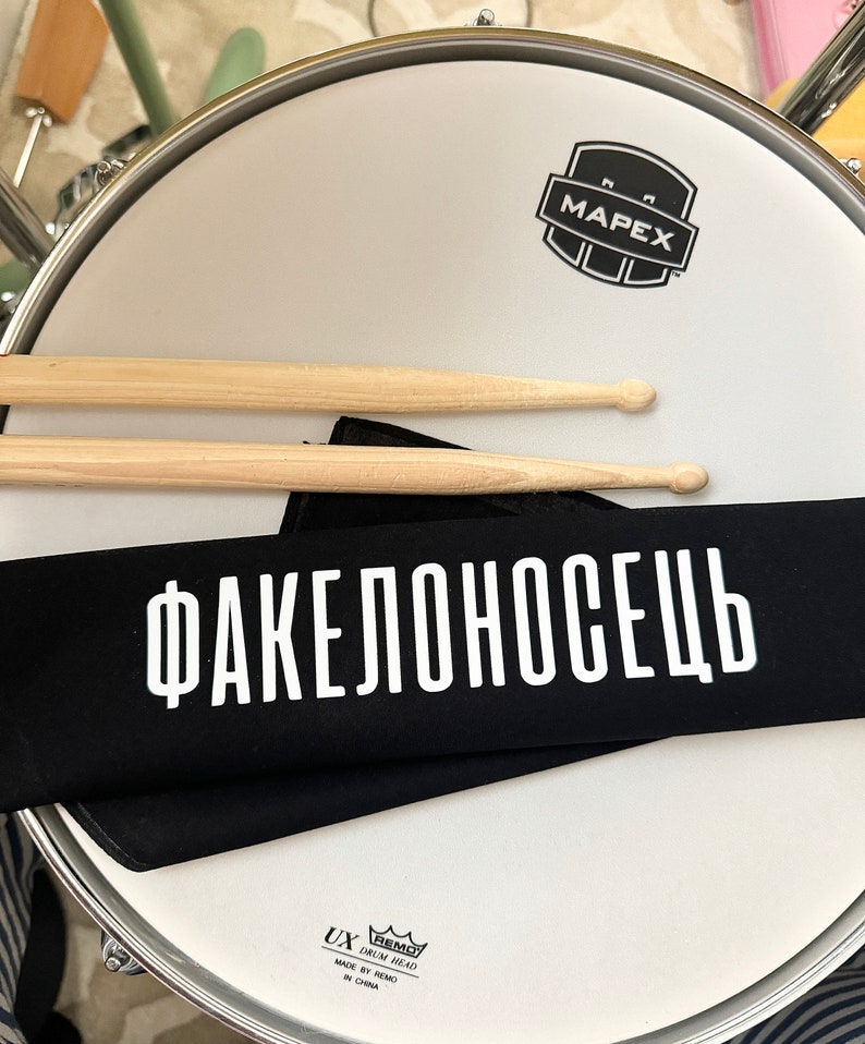 black bandana with white lettering sitting on a drum with drumsticks