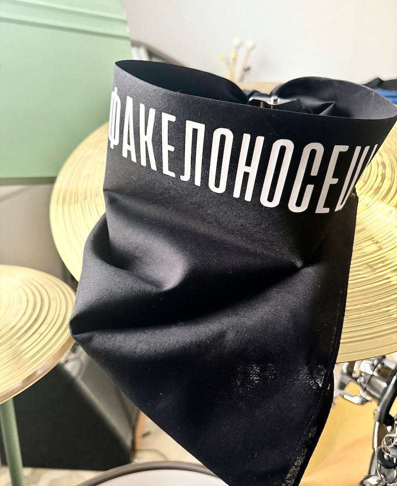 May include: Black bandana with the text "ФАКЕЛОНОСЕЦ" in white lettering.