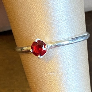 May include: A silver ring with a single red gemstone set in the center.