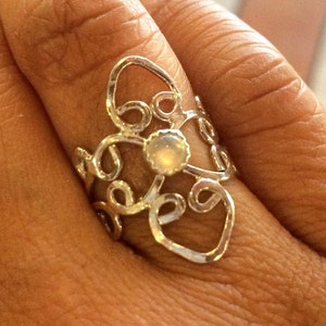 Puede incluir: Un anillo de plata con un diseño delicado y en espiral y una piedra preciosa blanca en el centro.