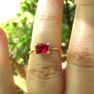 Może przedstawiać: Ręka z trzema złotymi pierścionkami. Pierścionek na palcu wskazującym ma czerwony kamień szlachetny. Pierścionek na środkowym palcu jest prostą obrączką. Pierścionek na małym palcu ma delikatny, falisty wzór.