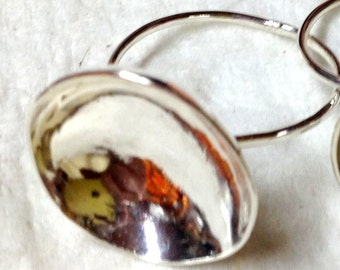 May include: A pair of silver hoop earrings with a unique, rounded, and slightly concave design. The earrings are made of polished silver and have a reflective surface.