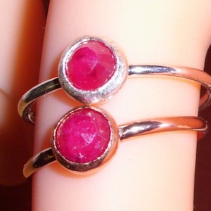 May include: Two silver rings with red ruby gemstones. The rings are stacked on top of each other on a finger.