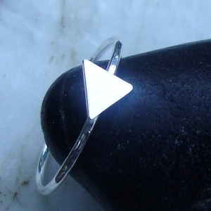 Puede incluir: Un anillo de plata con un diseño en forma de triángulo. El anillo está sobre una roca negra.